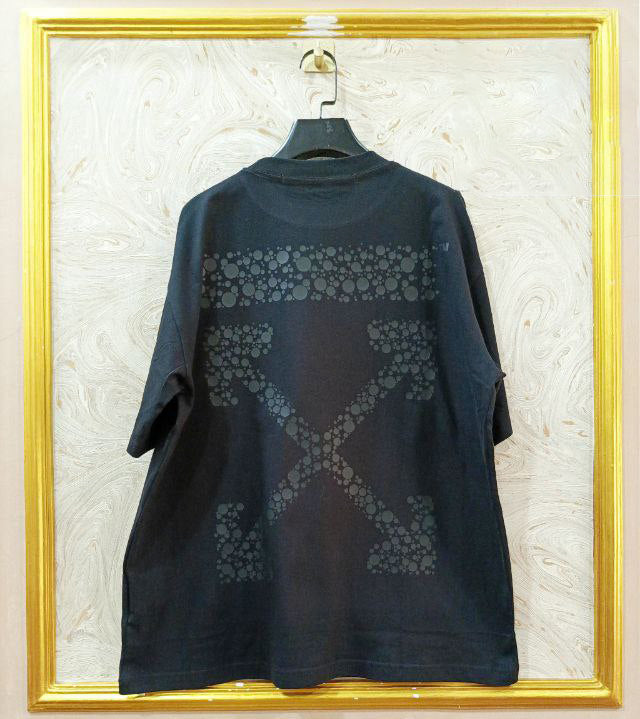 Black t-shirt with "Off-White™" design on a hanger against a decorative wall.