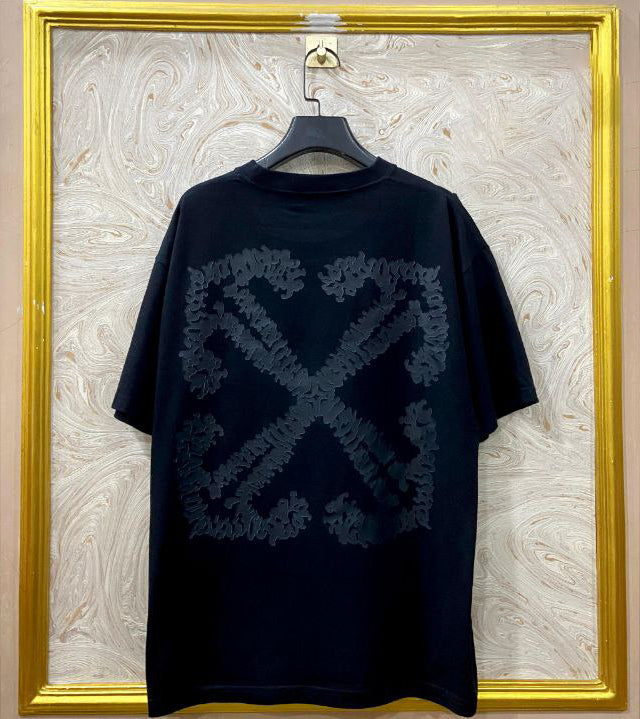 Black t-shirt with "Off-White™" design on a hanger against a decorative wall.