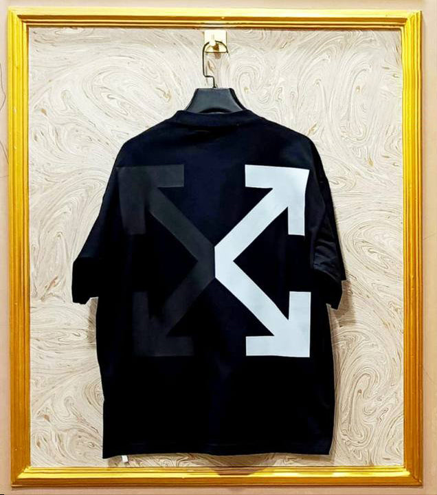 Black shirt with white logo on a mannequin against a decorative wall.