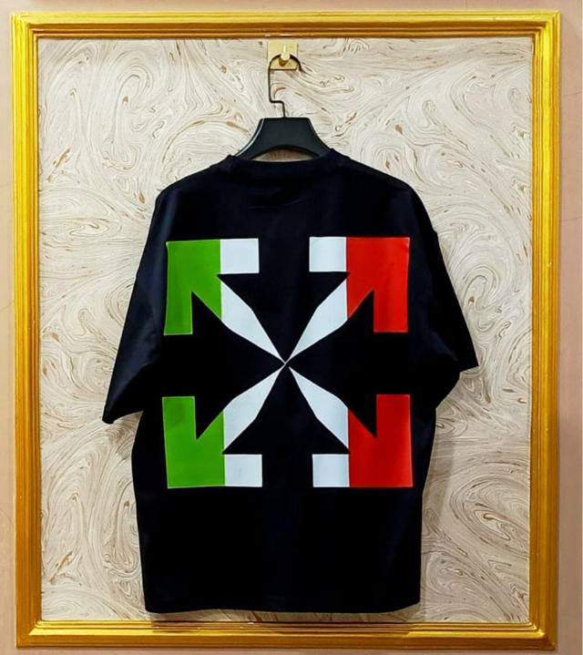 Black t-shirt with flag "Off-White™" design on a hanger against a decorative wall.