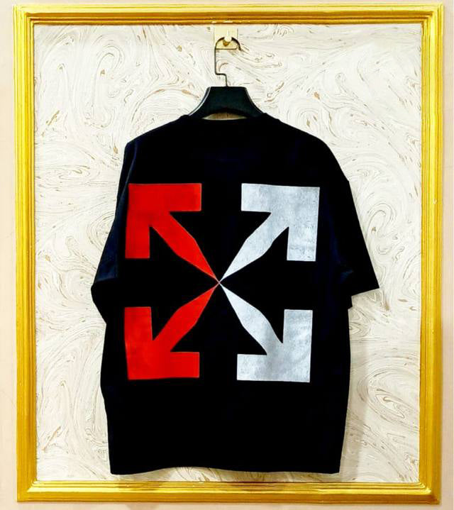 Black t-shirt with flag "Off-White™" design on a hanger against a decorative wall.