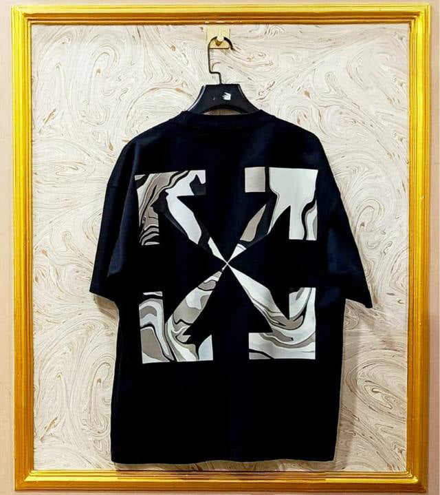 Black t-shirt with "Off-White™" design on a hanger against a decorative wall.