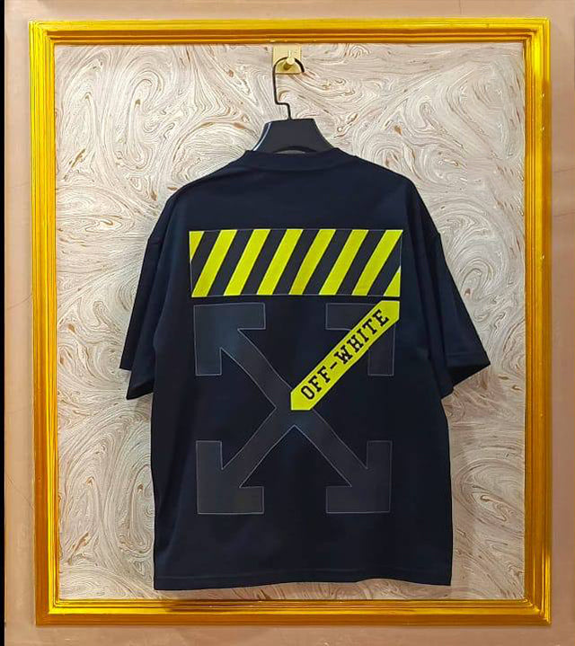Black t-shirt with "Off-White™" design on a hanger against a decorative wall.