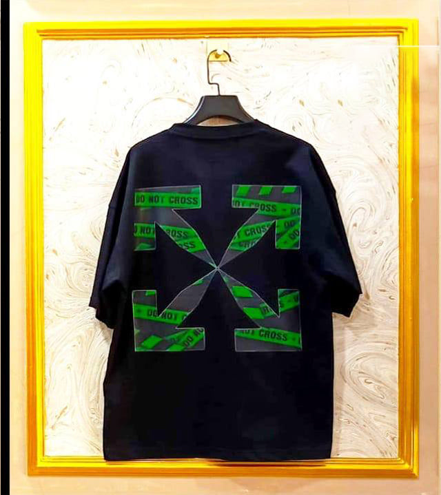 Black t-shirt with "Off-White™" design on a hanger against a decorative wall.