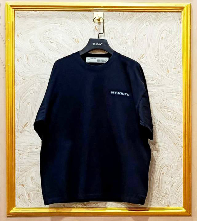 Black t-shirt with "Off-White™" logo on a hanger against a marble wall.