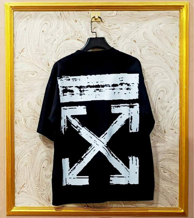 Black t-shirt with "Off-White™" design on a hanger against a decorative wall.