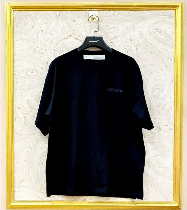 Black t-shirt with "Off-White™" logo on a hanger against a marble wall.