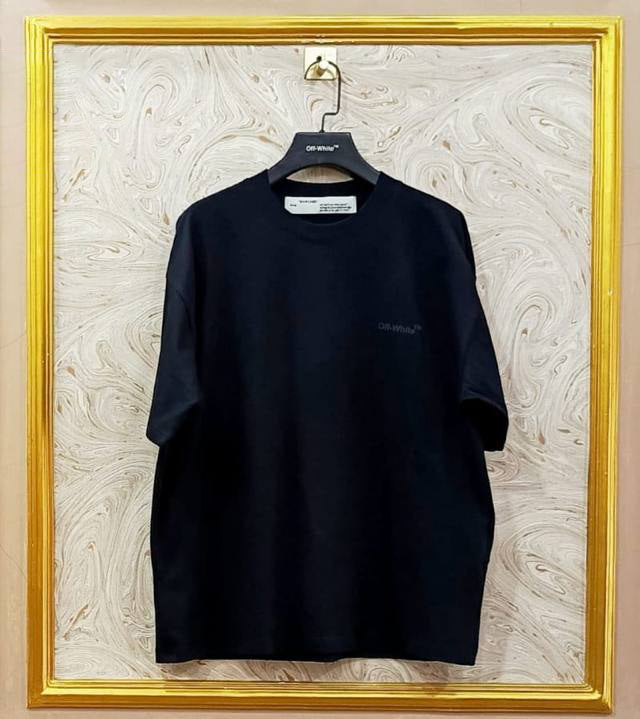 Black t-shirt with "Off-White™" logo on a hanger against a marble wall.