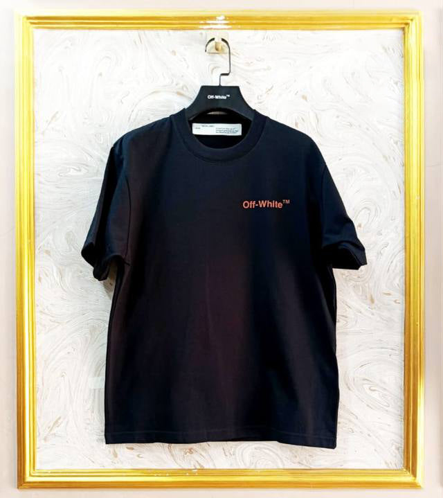 Black t-shirt with "Off-White™" logo on a hanger against a marble wall.