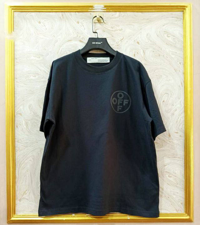 Black t-shirt with "Off-White™" logo on a hanger against a marble wall.