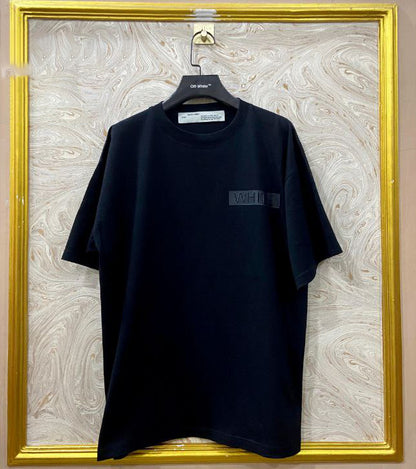 Black t-shirt with "Off-White™" logo on a hanger against a marble wall.