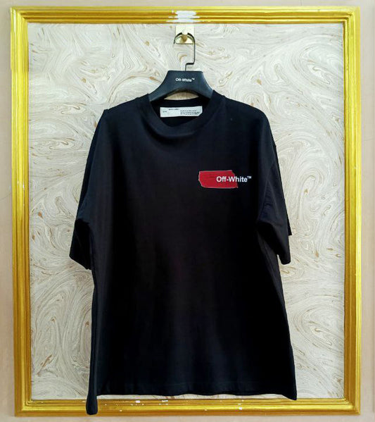 Black t-shirt with "Off-White™" logo on a hanger against a marble wall.