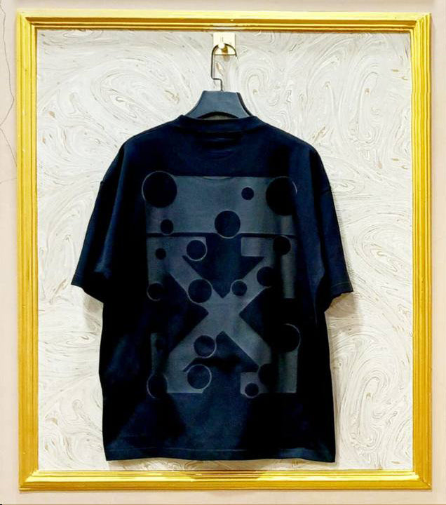 Black t-shirt with geometric design on a hanger against a textured wall.