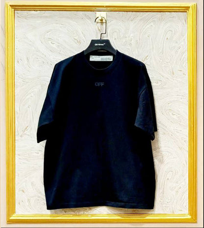 Black t-shirt with a logo on a hanger against a textured white wall.