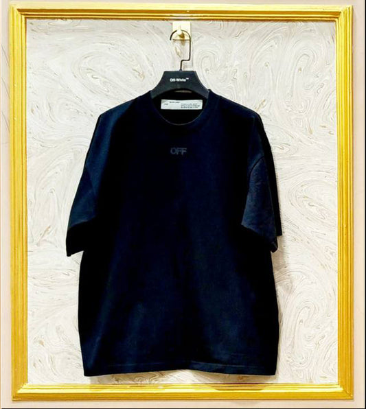 Black t-shirt with a logo on a hanger against a textured white wall.