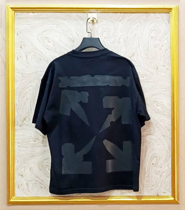 Black t-shirt with abstract designs on a hanger against a textured wall.