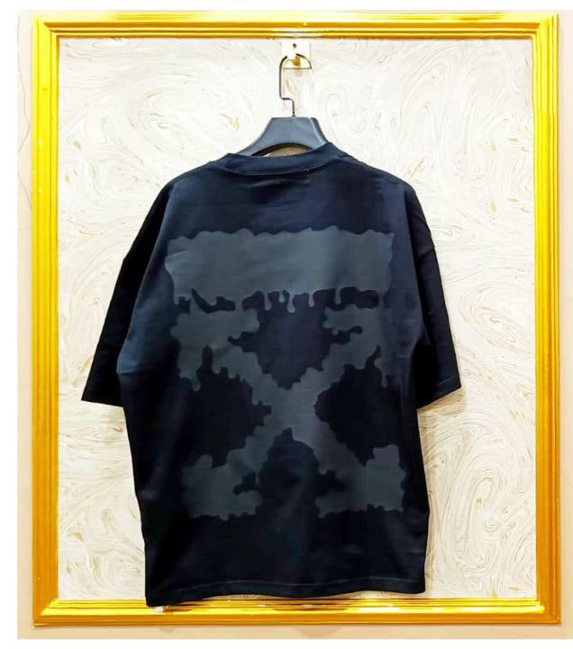 Black camouflage-patterned shirt on a hanger against a textured wall with a gold frame.