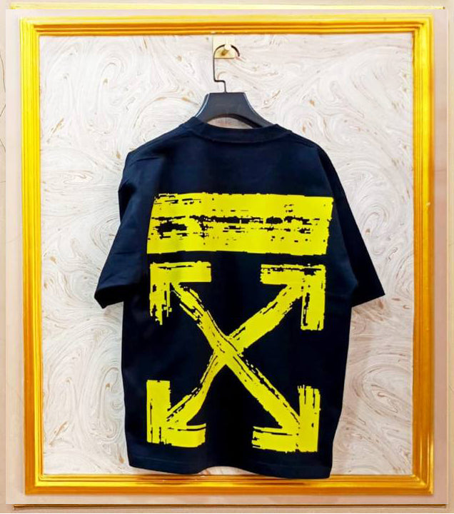 Black t-shirt with yellow graphic design on a hanger against a textured wall.