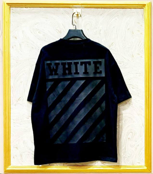 Black t-shirt with 'WHITE' text on a hanger against a textured white wall.