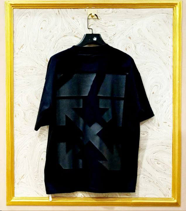 Black t-shirt with geometric design on a hanger against a textured wall.