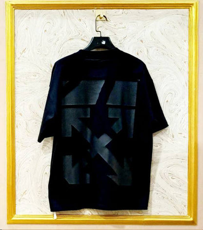 Black t-shirt with geometric design on a hanger against a textured wall.