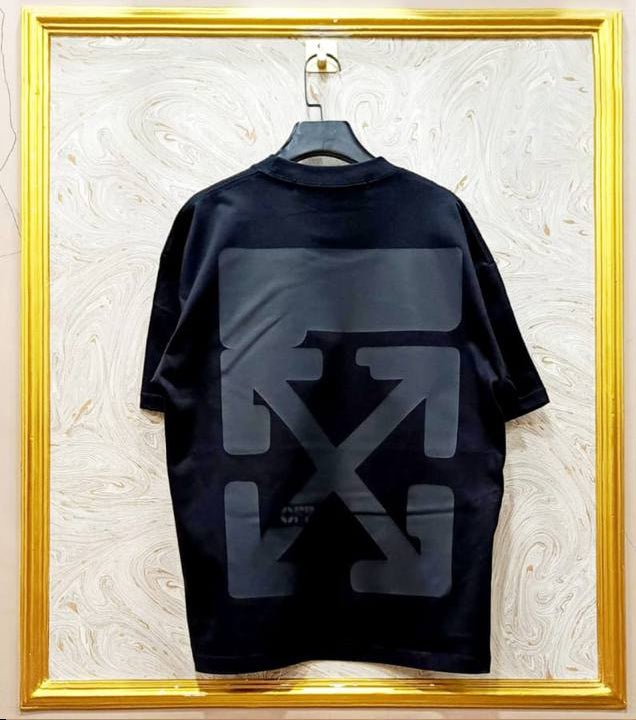 Black t-shirt with a logo on a hanger against a textured white wall.