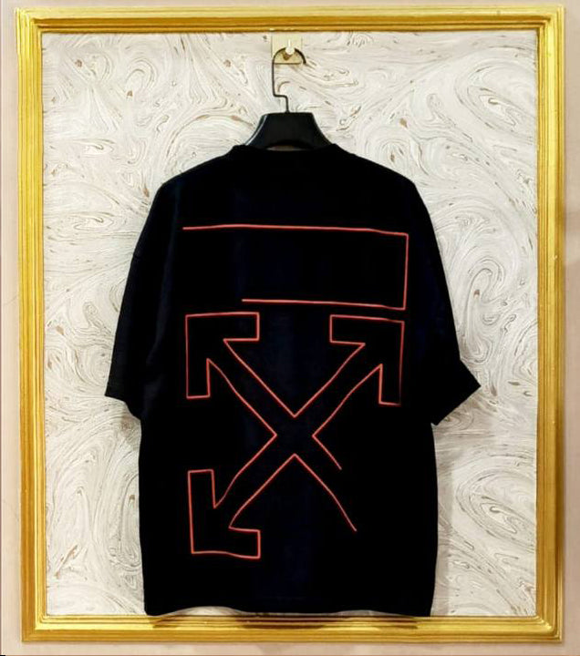 Black t-shirt with red geometric "Off-White™" design on a hanger against a decorative wall.