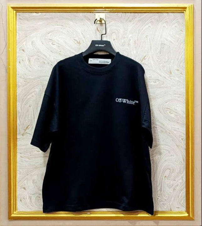 Black t-shirt with white "Off-White™" logo on a hanger against a marble wall.