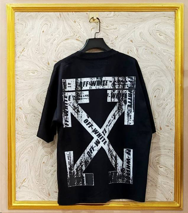 Black t-shirt with white graphic design on a hanger against a marble wall.