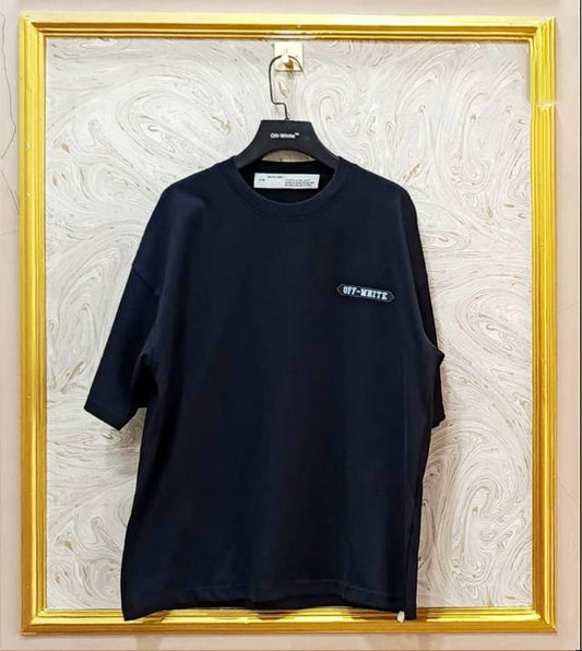 Black t-shirt with a logo on a hanger against a decorative wall.