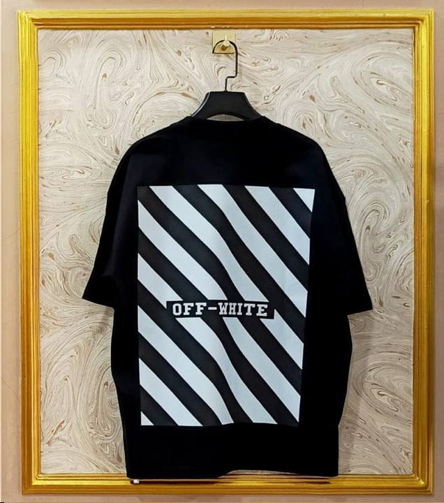 Black t-shirt with white geometric "Off-White™" design on a hanger against a decorative wall.