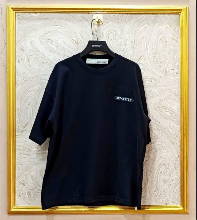 Black t-shirt with white "Off-White™" logo on a hanger against a marble wall.