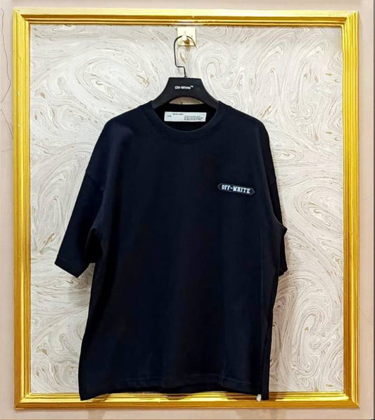 Black t-shirt with white "Off-White™" logo on a hanger against a marble wall.