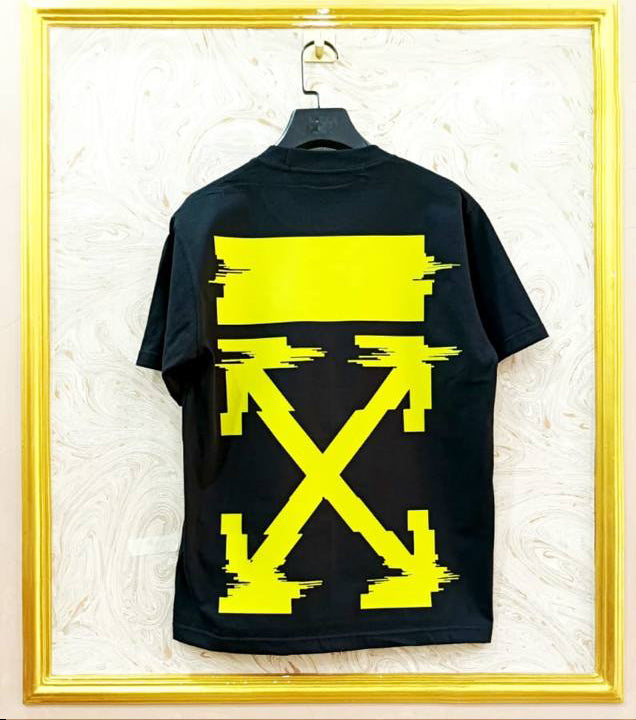 Black t-shirt with yellow graphic design on a hanger against a textured white wall.