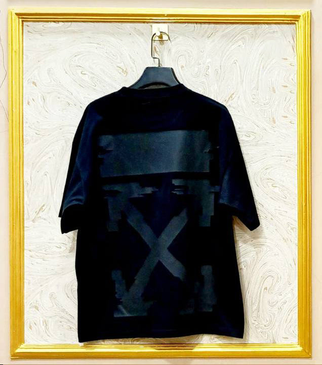 Black t-shirt with graphic design on a hanger against a textured white wall.