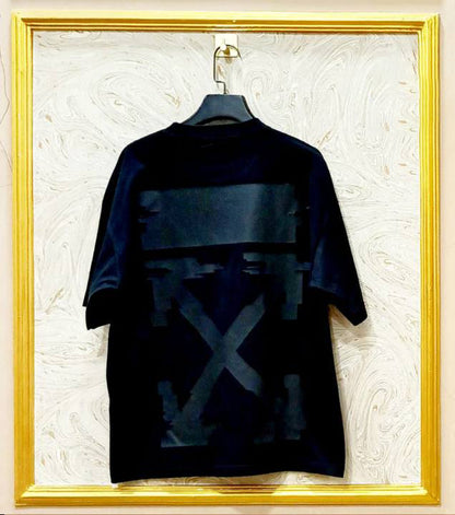 Black t-shirt with graphic design on a hanger against a textured white wall.