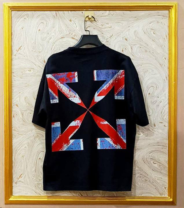 Black t-shirt with red, white, and blue geometric design on a hanger against a marble wall.