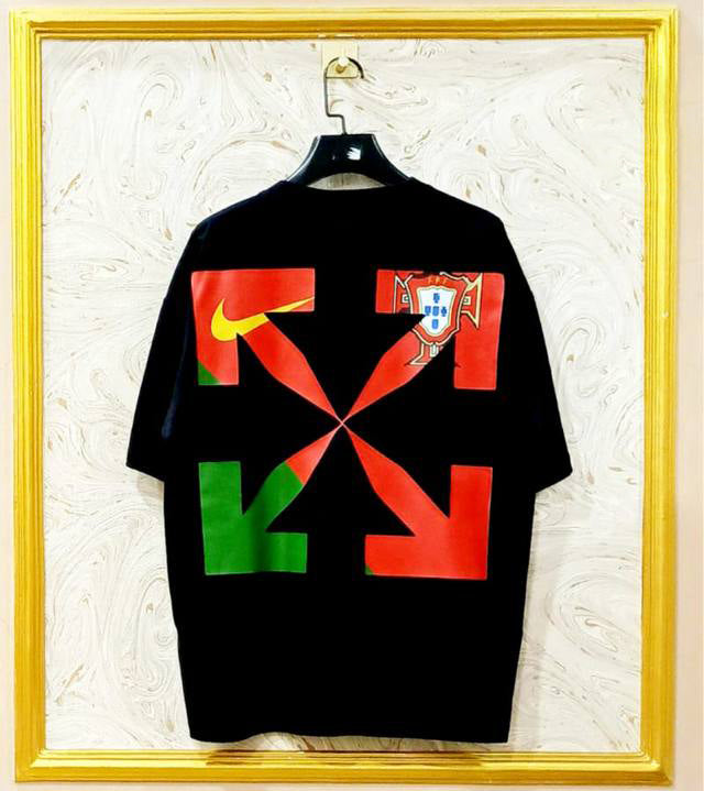 Black t-shirt with flag "Off-White™" design on a hanger against a decorative wall.