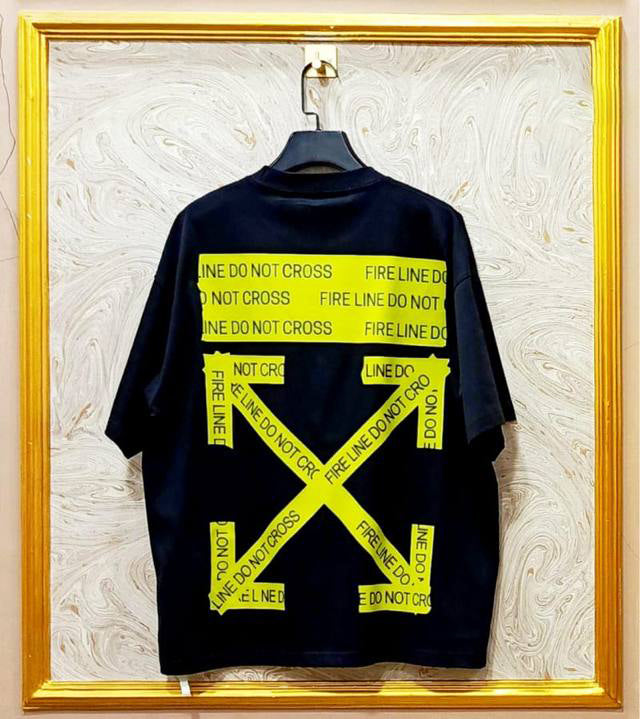 Black t-shirt with "Off-White™" design on a hanger against a decorative wall.