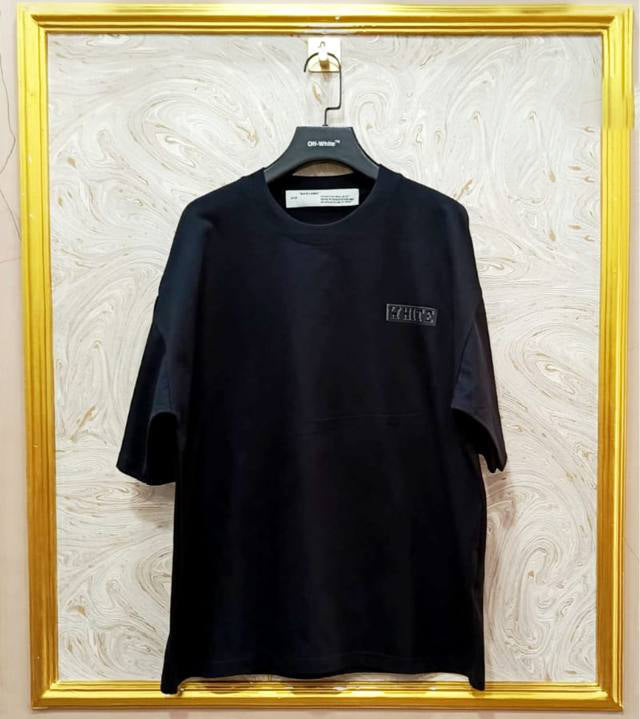 Black t-shirt with "Off-White™" logo on a hanger against a marble wall.