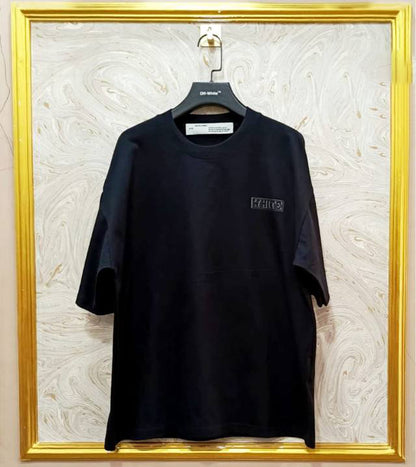 Black t-shirt with "Off-White™" logo on a hanger against a marble wall.