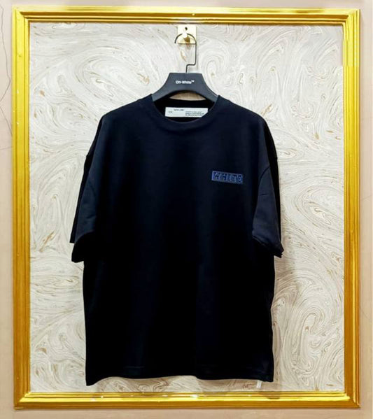 Black t-shirt with "Off-White™" logo on a hanger against a marble wall.